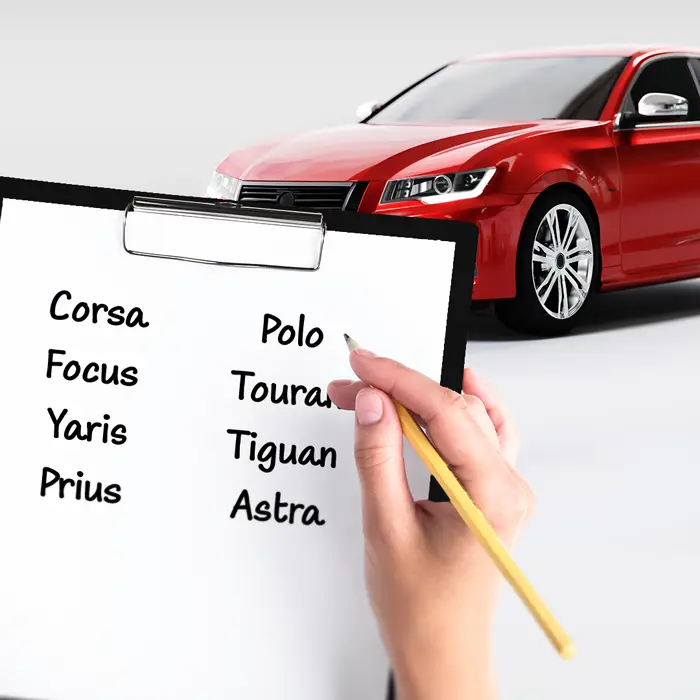 Im Vordergrund ist eine Klemmmappe mit einem weißen Blatt Papier, auf dem Modellnamen verschiedener Autohersteller geschrieben stehen. Rechts daneben hält eine Hand einen Bleistift. Der Hintergrund dieser Szene ist eine weiße Fläche, mit einem roten Auto, welches durch die Klemmmappe leicht verdeckt wird.