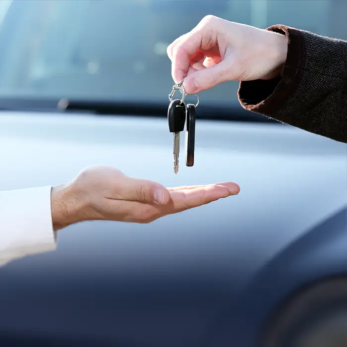 Beim Autoverkauf wechselt der Fahrzeugschlüssel den Besitzer. Eine von der rechten Bildseite kommende Hand hält den Schlüssel mit 2 Fingern. Unter dem Schlüssel schwebt eine nach oben offene Hand, die den Schlüssel in Empfang nehmen möchte.