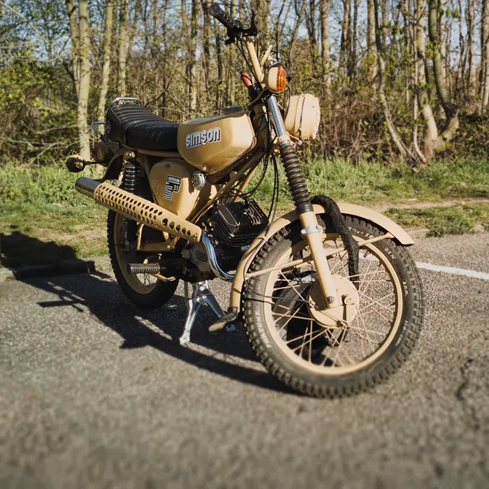 Das Kult-Moped der DDR, eine Simson S 51 in der Farbe gold-beige, posiert auf einem asphaltierten Feldweg.