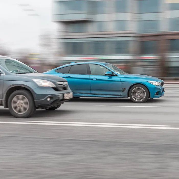 Ein türkisfarbener BMW und ein grauer Honda SUV fahren mit hoher Geschwondigkeit im Stadtgebiet offenbar ein illegales Autorennen.