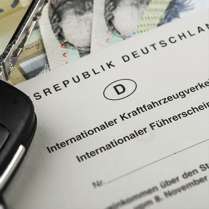 Auf einem im Anschnitt zu sehen internationalen Führerschein in deutscher Sprache liegt ein schwarzer Autoschlüssel.