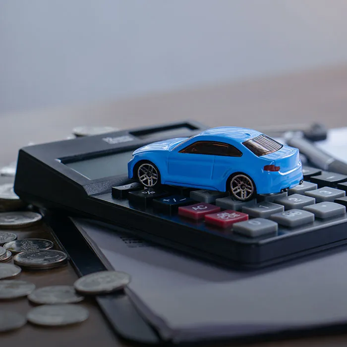 Symbolbild für die Pendlerpauschale: ein blaues Miniaturauto steht auf einem Taschenrechner. Daneben liegen verschiedene Münzen.
