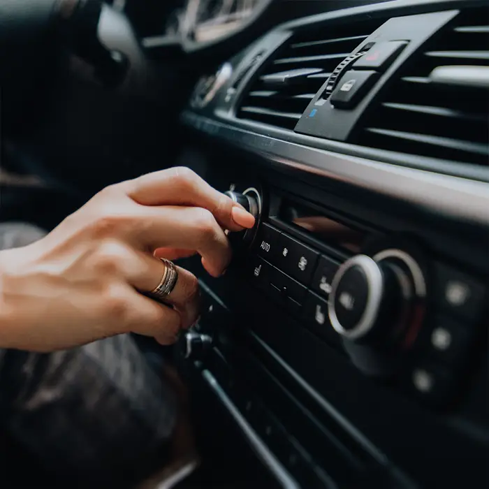 Eine weibliche Hand sucht im Auto den Drehregler Ihres Soundsystems.